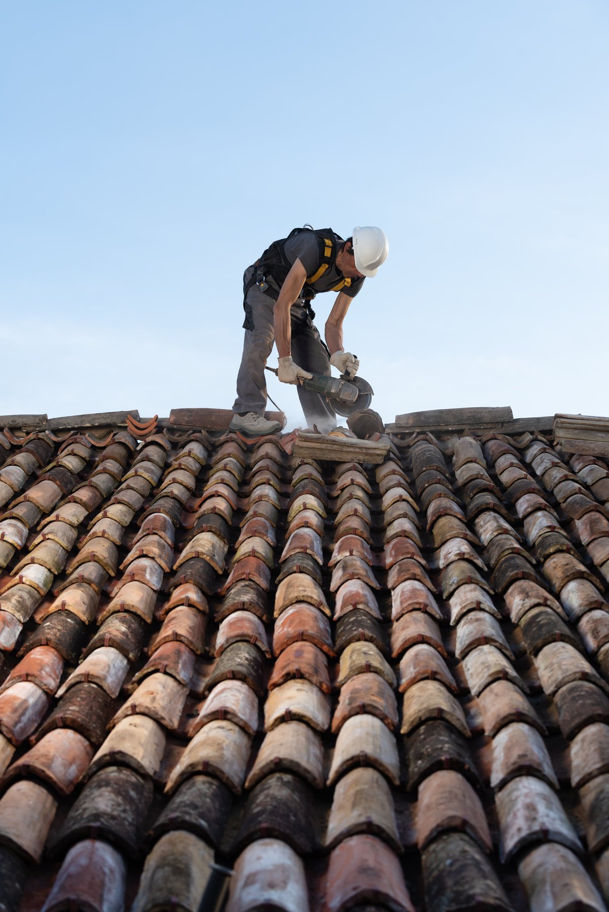 Professional roofer working on a clay tile roof, secured with a safety harness